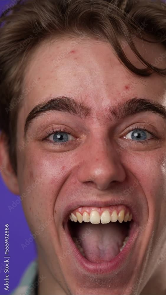 Vertical video closeup slow motion excited jubilant overjoyed young man 20s doing winner gesture celebrate clenching fists say yes isolated on purple background studio portrait Vertical video closeup slow motion excited jubilant overjoyed young man 20s doing winner gesture celebrate clenching fists say yes isolated on purple background studio portrait