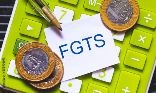 As iniciais FGTS de Fundo de Garantia do Tempo de Serviço escritas em um pedaço de papel sobre uma calculadora com moedas do Brasil na composição. photo