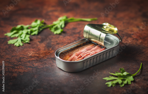 Canned anchovies open on a dark brown table with parsley. Ready for eat. 