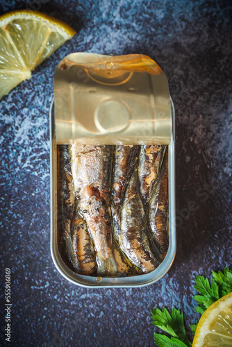 Canned sardines with olive oil open on a dark blue table with lemon and parsley. Ready for eat. 