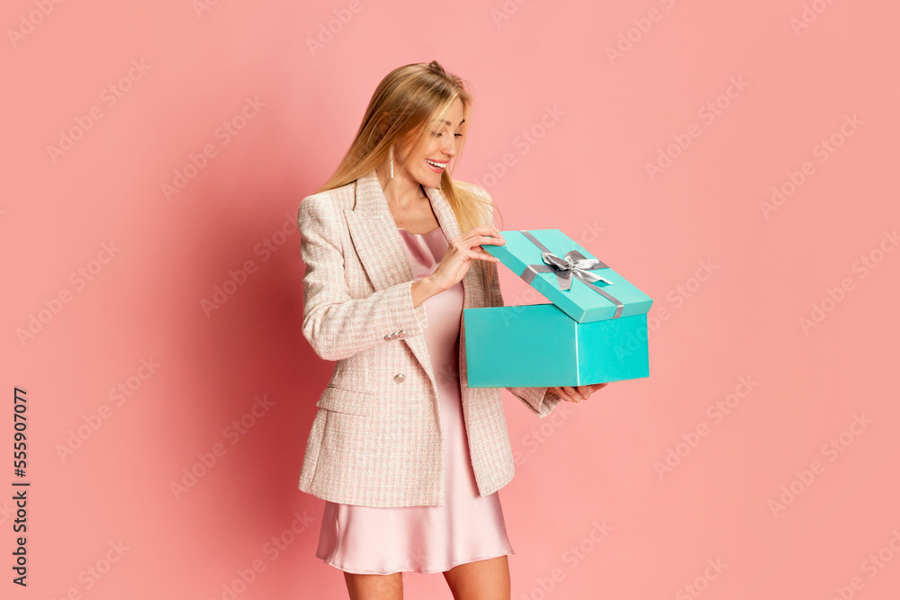 Portrait of beautiful young woman posing, opening present box over pink background. Surprise. Holidays, celebration and women concept Portrait of beautiful young woman posing, opening present box over pink background. Surprise. Holidays, celebration and women concept