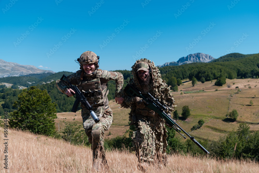 A sniper team squad of soldiers is going undercover. Sniper assistant and team leader walking and aiming in nature with yellow grass and blue sky. Tactical camouflage uniform. A sniper team squad of soldiers is going undercover. Sniper assistant and team leader walking and aiming in nature with yellow grass and blue sky. Tactical camouflage uniform.