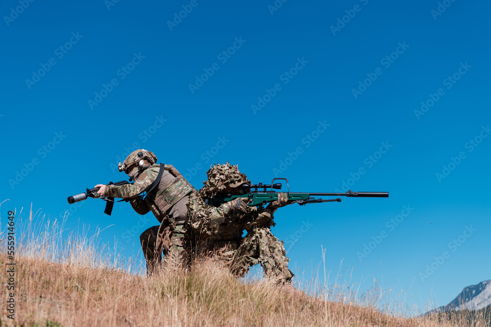 A sniper team squad of soldiers is going undercover. Sniper assistant and team leader walking and aiming in nature with yellow grass and blue sky. Tactical camouflage uniform. A sniper team squad of soldiers is going undercover. Sniper assistant and team leader walking and aiming in nature with yellow grass and blue sky. Tactical camouflage uniform.