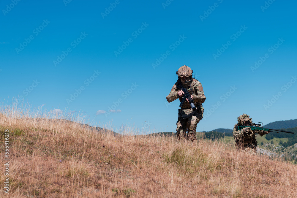 A sniper team squad of soldiers is going undercover. Sniper assistant and team leader walking and aiming in nature with yellow grass and blue sky. Tactical camouflage uniform. A sniper team squad of soldiers is going undercover. Sniper assistant and team leader walking and aiming in nature with yellow grass and blue sky. Tactical camouflage uniform.