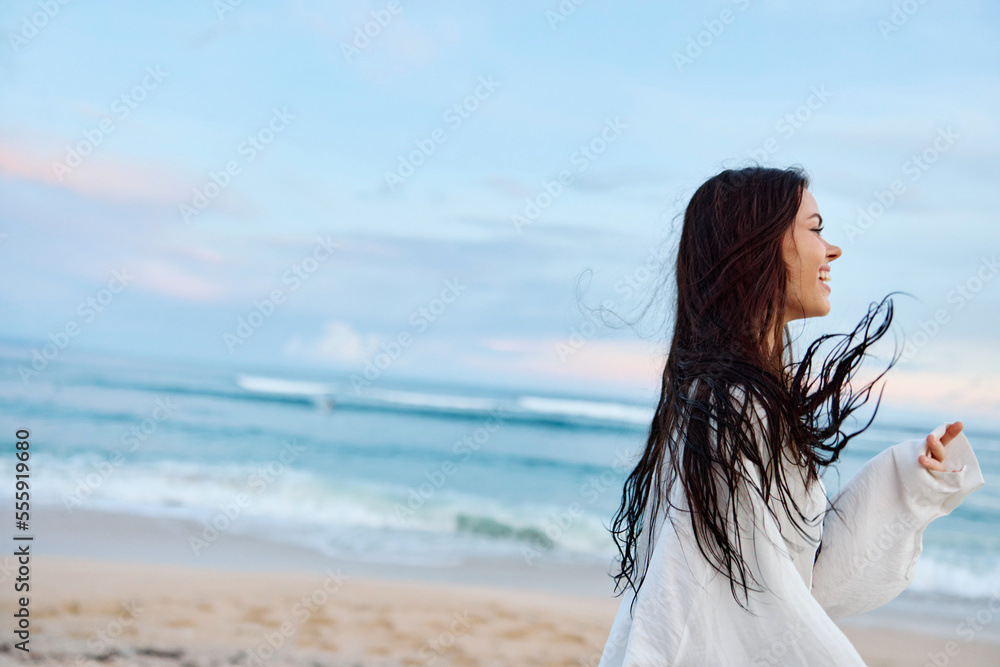 Obraz premium Brunette woman with long hair in a white shirt and denim shorts smile and happiness running on the beach and having fun smile with teeth in front of the ocean, vacation summer trip