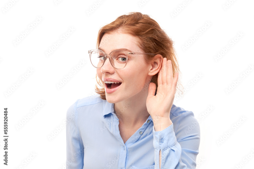 Young redhead woman in business shirt smiling and holding hand near ear, listening carefully, hearing intently isolated on white background Young redhead woman in business shirt smiling and holding hand near ear, listening carefully, hearing intently isolated on white background