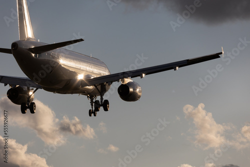 close-up of a silver aircraft in final approach at Stuttgart Airport, against bright cloudy sky. Reflection of the sun in the aircraft, landing gear down