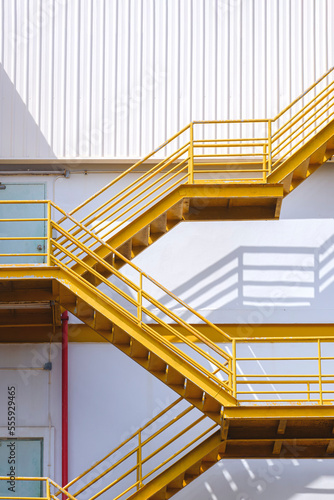 Yellow fire escape on white corrugated steel wall outside of industrial building in vertical frame