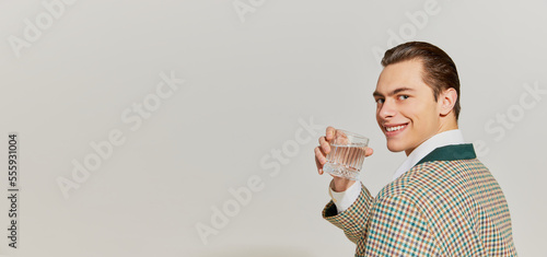 Photography Flyer with young handsome man in vintage old-fashioned jacket drinking water with charming smile over grey background