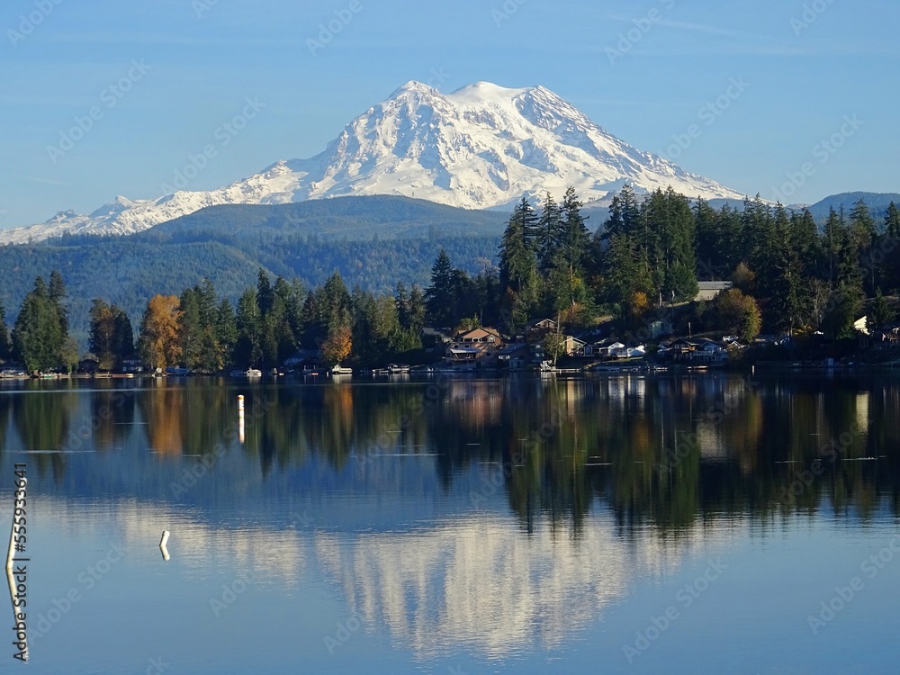 Mount rainier and its reflection in a lake, clear blue skies and autumn colors on the trees. Washington state, USA.