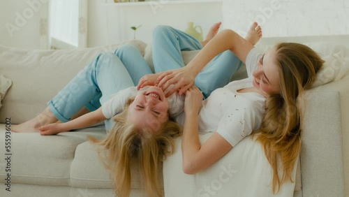 Caucasian mother mom with daughter lying on couch sofa in living room mommy tickle kid girl laughing tickling child baby sincere funny laugh enjoy playing fun game play together family weekend at home