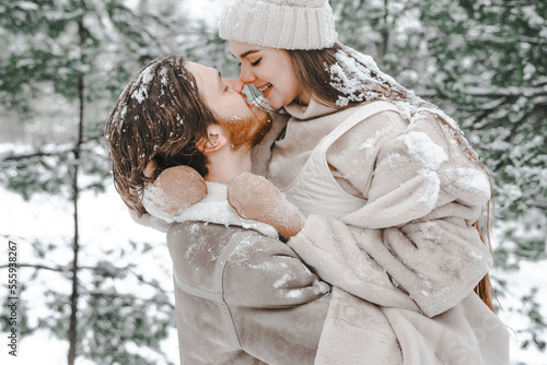 Romantic snow love story.Young couple guy girl playing kissing in snowy winter forest with trees.Walking,having fun,laughing in stylish warm clothes,fur coat,woole jacket,shawl.Date,vacation weekend photo