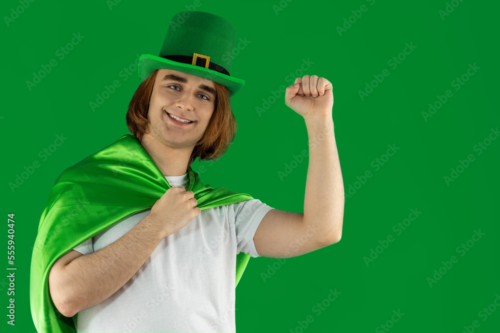 Young man celebranting St. Patrick's Day. Portrait of guy Prep Student with long hair wearing green Leprechaun hat and green cape Young man celebranting St. Patrick's Day. Portrait of guy Prep Student with long hair wearing green Leprechaun hat and green cape