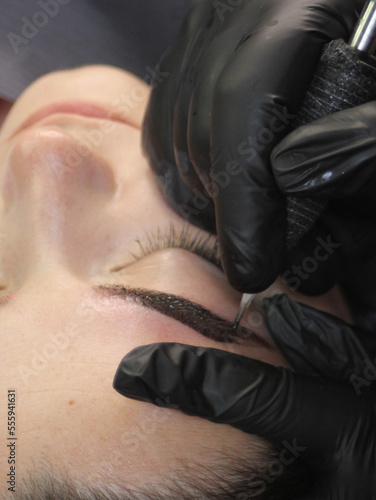 Cosmetologist applying permanent make up eyebrows for a client in a salon. Microblading technique.