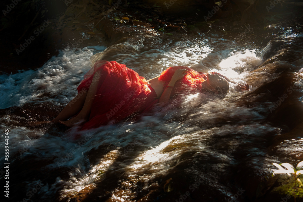 Asian woman in red dress sleeping in hill waterfall at evening