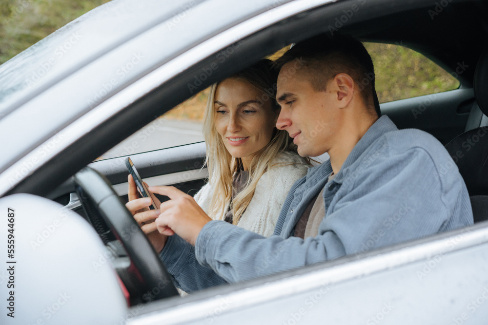 A young couple on a road trip looking at a map on their phone in a navigator. A young couple on a road trip looking at a map on their phone in a navigator.