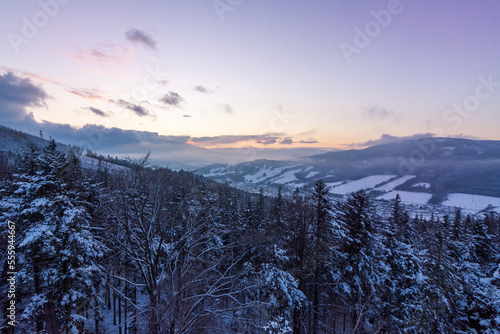 View of snow-covered trees and mountains at sunset from the viewpoint of Certovy kameny in Jeseniky mountains in Czech republic. photo