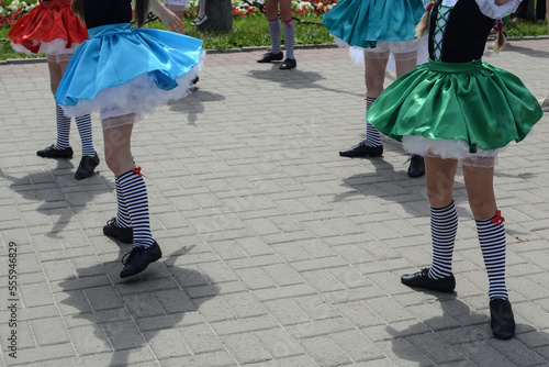 Legs of little girls dancers in high striped socks and black dance shoes against a background of paving slabs.