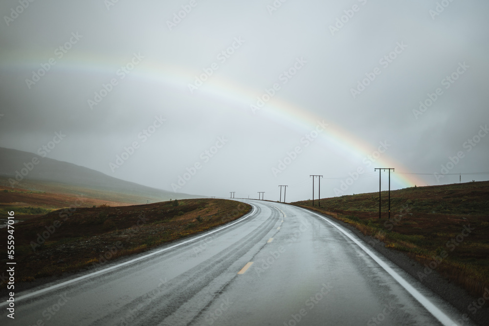 Landscape with an empty road in northern Norway on a moody autumn day with a rainbow background