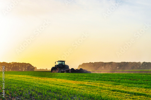 the tractor plows the ground in the spring in the field before planting the grain. Morning dawn in the field. High quality photo