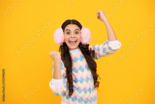 Excited face. Fashion happy young woman in winter warm earmuff ear-flaps hat and sweater having fun over colorful blue background Amazed expression, cheerful and glad.