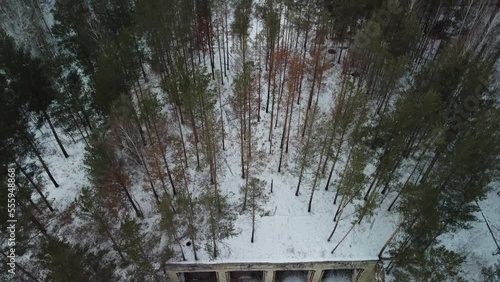 Flying a drone over an abandoned military garage in the forest in winter. 4K video.