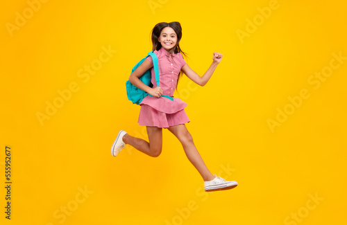 School girl in school uniform with school bag. Crazy run and jump. Schoolchild teenager hold backpack on yellow isolated background.