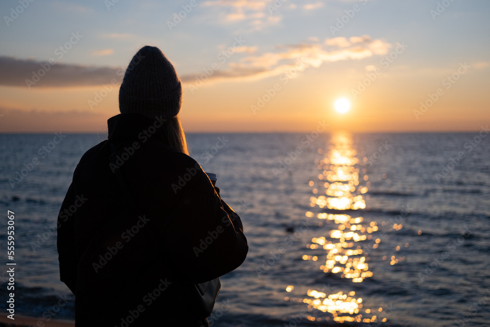 People drink cup of coffee during sunset on the beach in winter blurred