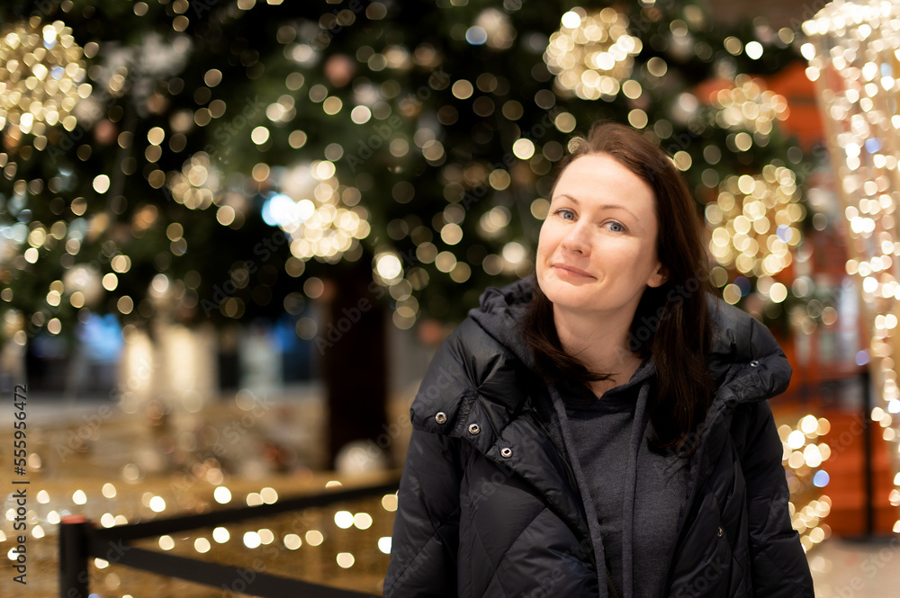 Portrait of a beautiful woman on the background of a Christmas tree with bright lights gerlant. Beautiful multicolored bokeh in the background