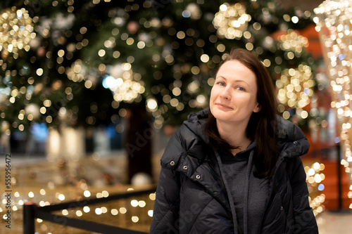 Portrait of a beautiful woman on the background of a Christmas tree with bright lights gerlant. Beautiful multicolored bokeh in the background