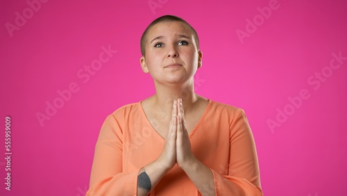 Fotografie, Obraz Gender fluid non binary woman 20s praying, make a wish, pleading, posing isolated on pink background studio