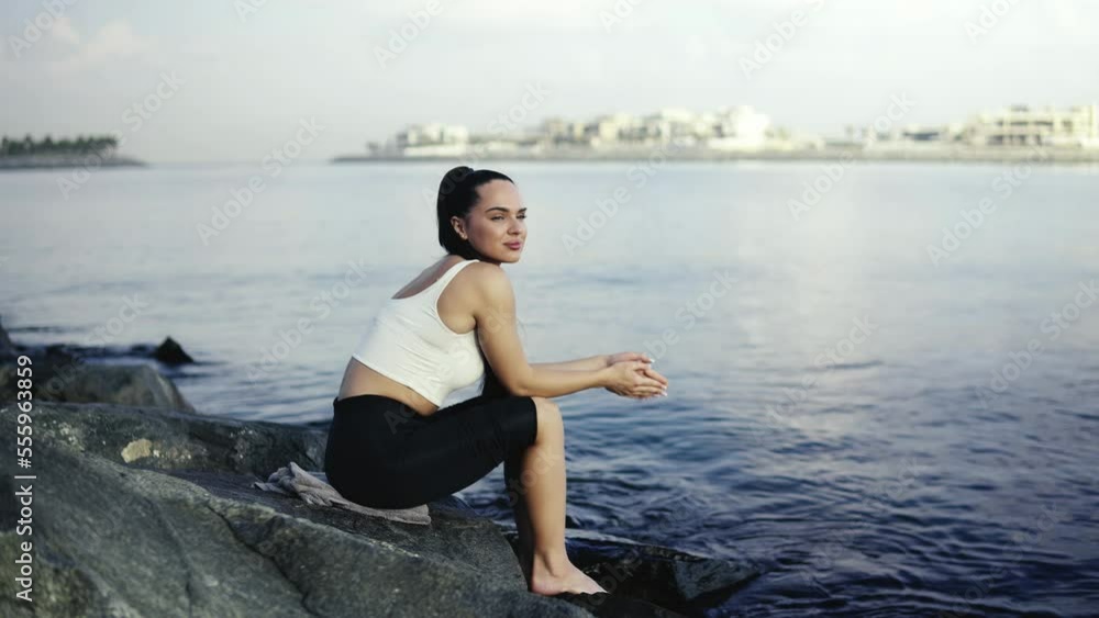 The girl sits on a stone near the shore enjoying the view of the water, bay and nature. Happy girl with long hairs relaxing on the sea. The girl sits on a stone near the shore enjoying the view of the water, bay and nature. Happy girl with long hairs relaxing on the sea.