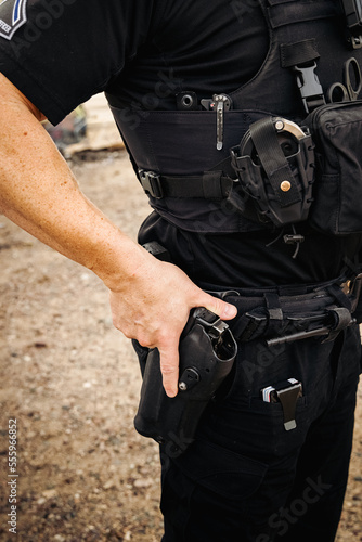 Vertical image of white male caucasian police officer reaching down and places hand on his weapon hand gun that is still in its holster on hip. Close up shot. No head.
