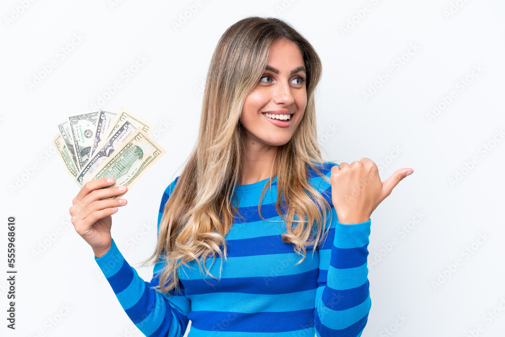 Young Uruguayan woman taking a lot of money isolated on white background pointing to the side to present a product Young Uruguayan woman taking a lot of money isolated on white background pointing to the side to present a product