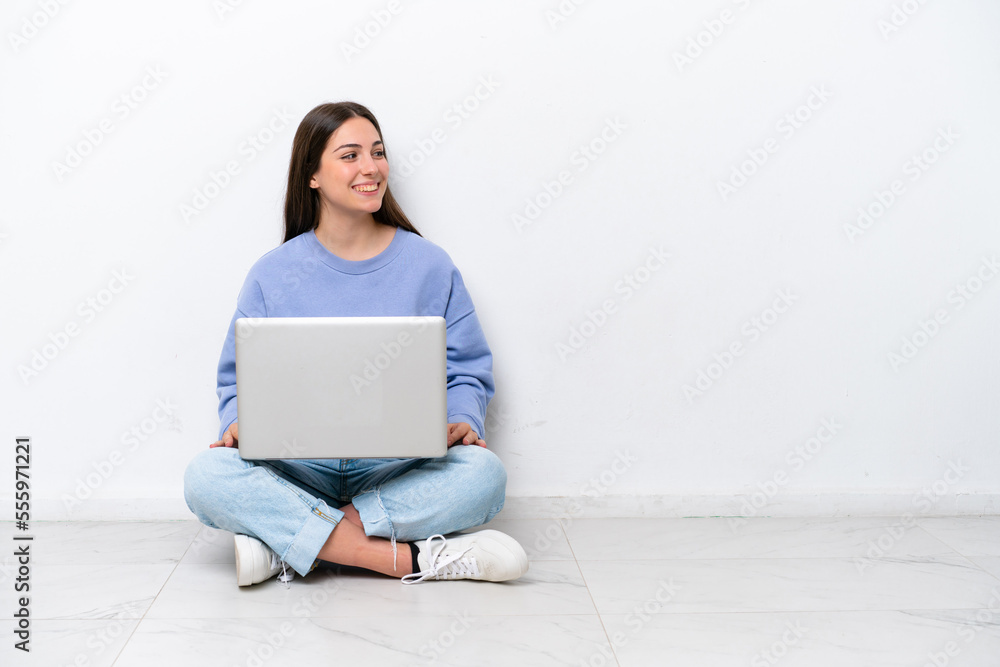 Young caucasian woman with laptop sitting on the floor isolated on white background looking side Young caucasian woman with laptop sitting on the floor isolated on white background looking side