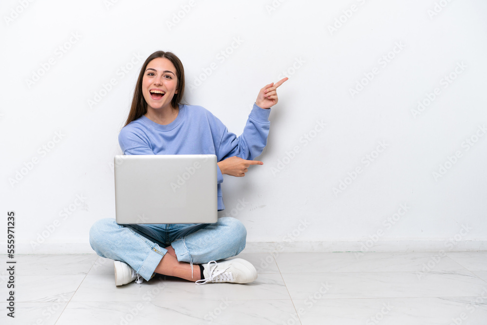 Young caucasian woman with laptop sitting on the floor isolated on white background surprised and pointing side Young caucasian woman with laptop sitting on the floor isolated on white background surprised and pointing side