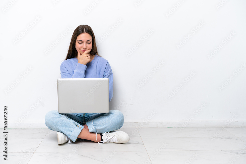 Young caucasian woman with laptop sitting on the floor isolated on white background looking to the side Young caucasian woman with laptop sitting on the floor isolated on white background looking to the side