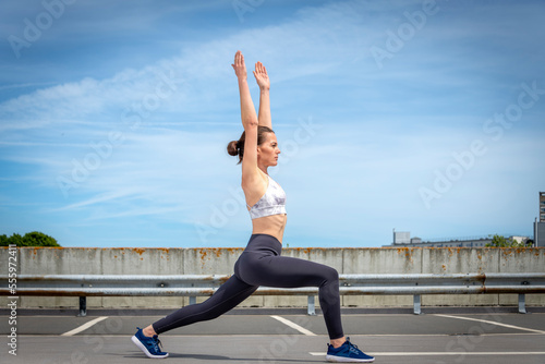 Sporty fit woman doing stretching exercise outside in the sun, urban setting.