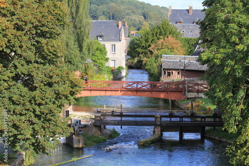 the river durdent in cany barville in seine maritime in normandy with a bridge and a weir and green trees and houses in summer