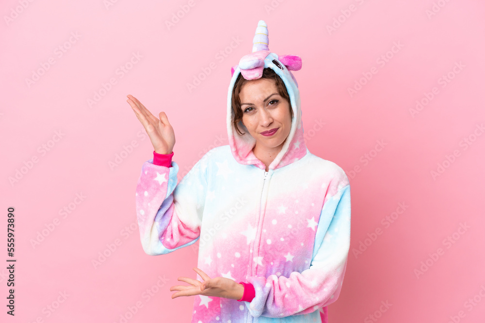 Young caucasian woman with unicorn pajamas isolated on pink background extending hands to the side for inviting to come Young caucasian woman with unicorn pajamas isolated on pink background extending hands to the side for inviting to come