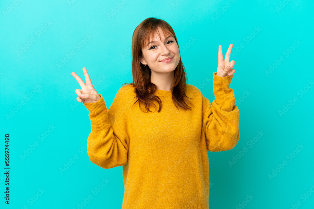 Redhead girl isolated on blue background showing victory sign with both hands Redhead girl isolated on blue background showing victory sign with both hands