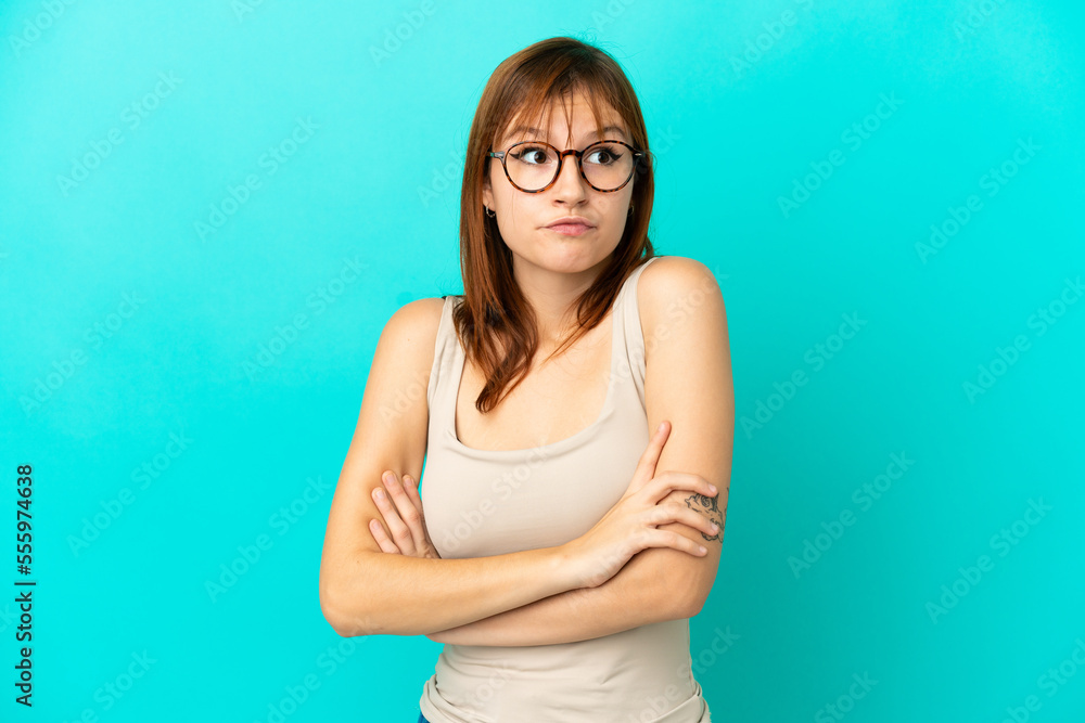 Redhead girl isolated on blue background making doubts gesture while lifting the shoulders Redhead girl isolated on blue background making doubts gesture while lifting the shoulders
