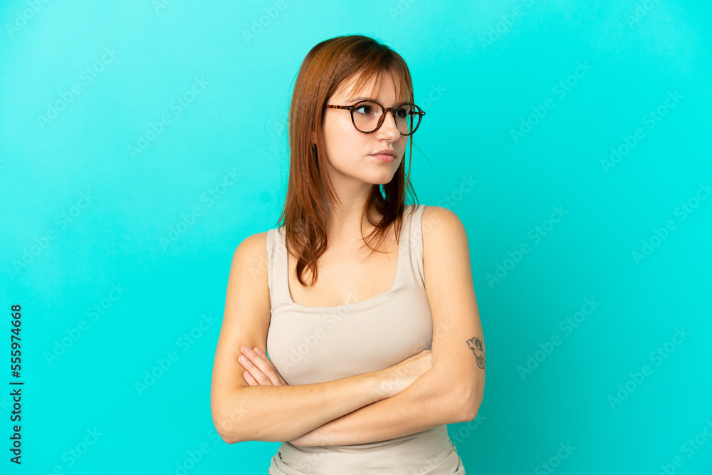 Redhead girl isolated on blue background keeping the arms crossed Redhead girl isolated on blue background keeping the arms crossed