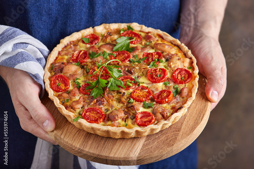 Quiche open tart with chicken meat, cherry tomatoes and parsley leaves. Savory taste. Man holding a dish with pie.