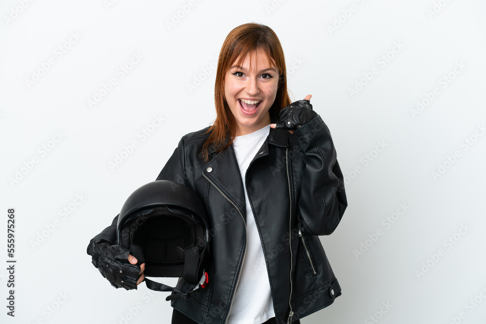 Redhead girl with a motorcycle helmet isolated on white background making phone gesture. Call me back sign Redhead girl with a motorcycle helmet isolated on white background making phone gesture. Call me back sign