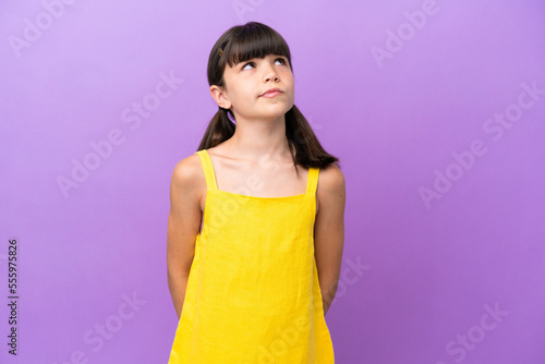 Little caucasian kid isolated on purple background and looking up