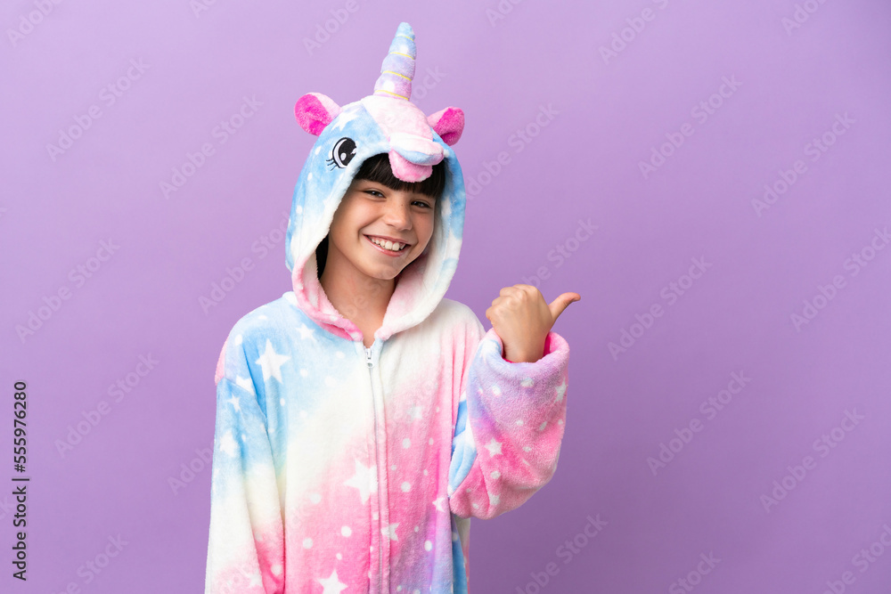 Little kid wearing a unicorn pajama isolated on purple background pointing to the side to present a product Little kid wearing a unicorn pajama isolated on purple background pointing to the side to present a product