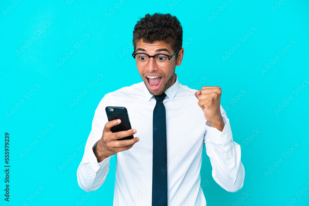 Young business Brazilian man isolated on blue background surprised and sending a message Young business Brazilian man isolated on blue background surprised and sending a message