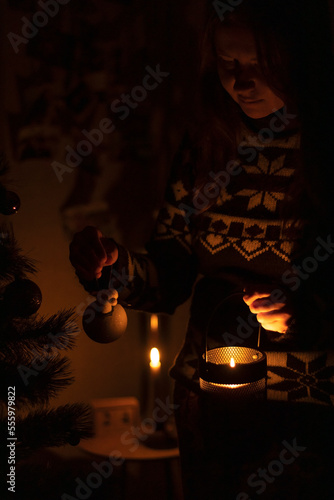 Ukraine, winter 2022. A woman decorates a Christmas tree in the dark with a candle.