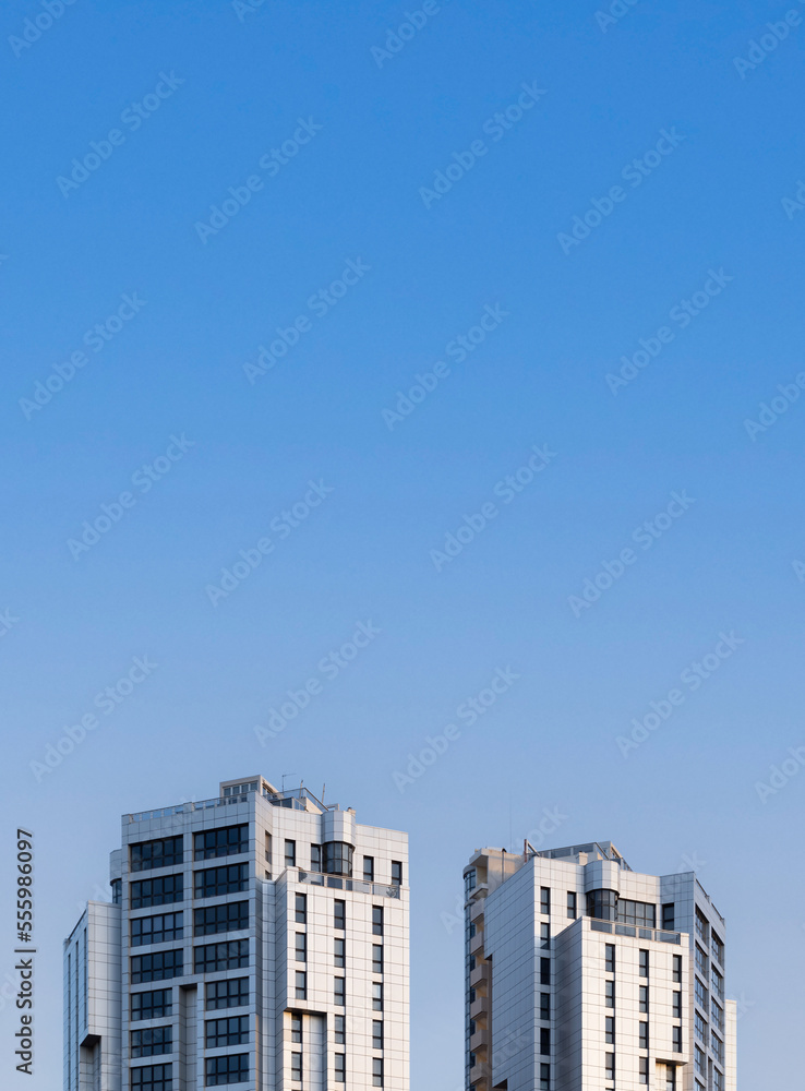 Front view of the top of two tall residential towers with blue sky and copy space